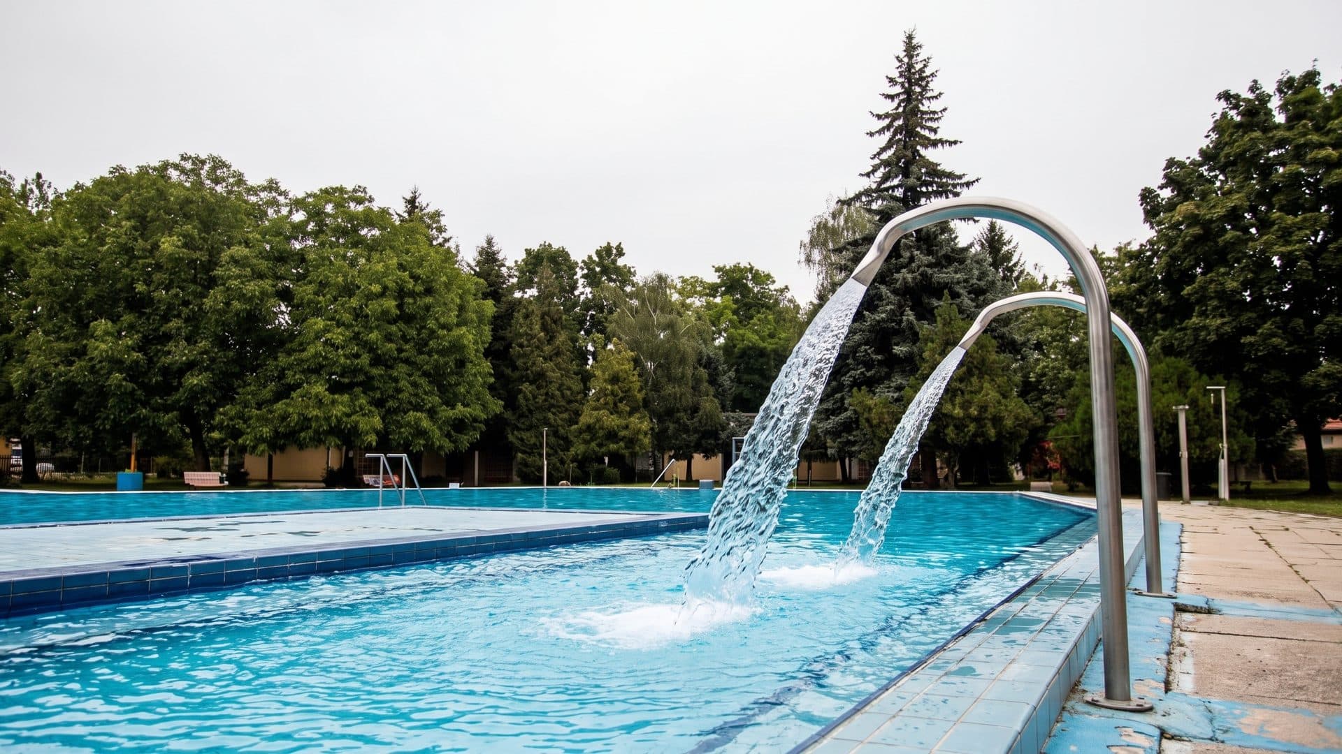 The outdoor pool at Tiszafured with its pair of arched water spouts, conifers behind
