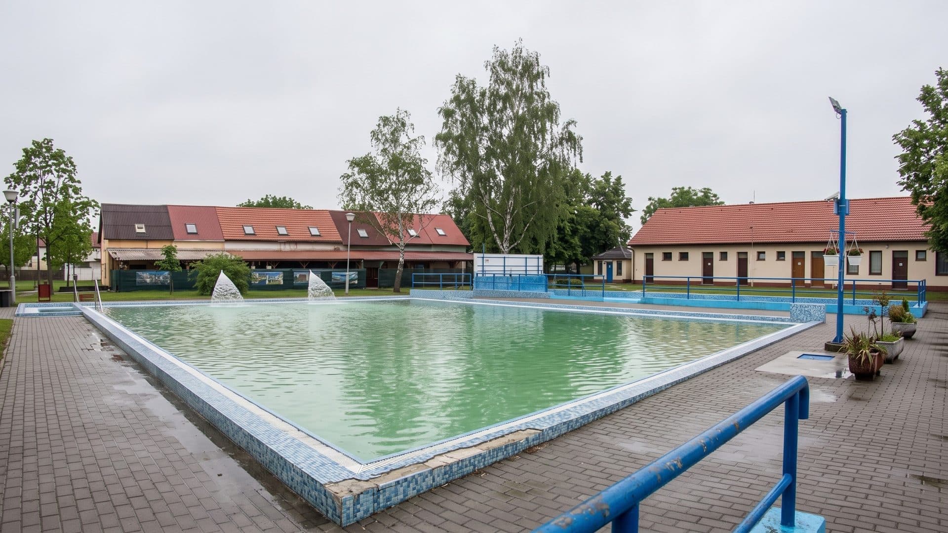 The open-air thermal pool of the Szent Andras baths in Toalmas with green mineral water, fountain jets and tiled-roof buildings behind