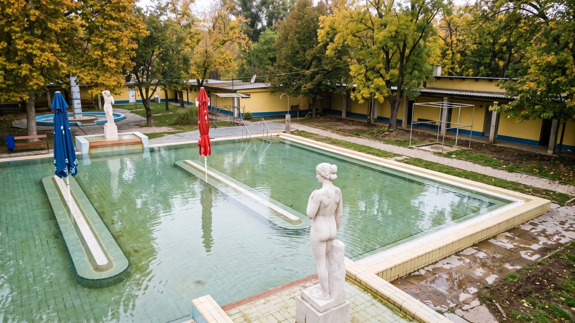 The open-air thermal pool of the Torok Sandor baths in Hodmezovasarhely with a white statue and parasols among autumn trees