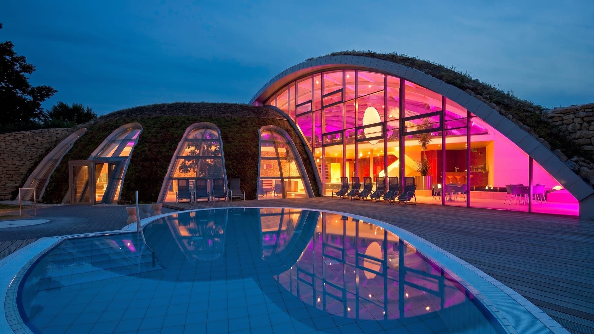 The shell-shaped roof of the Toskana Therme in Bad Sulza at dusk, lit from within and reflected in the outdoor pool.