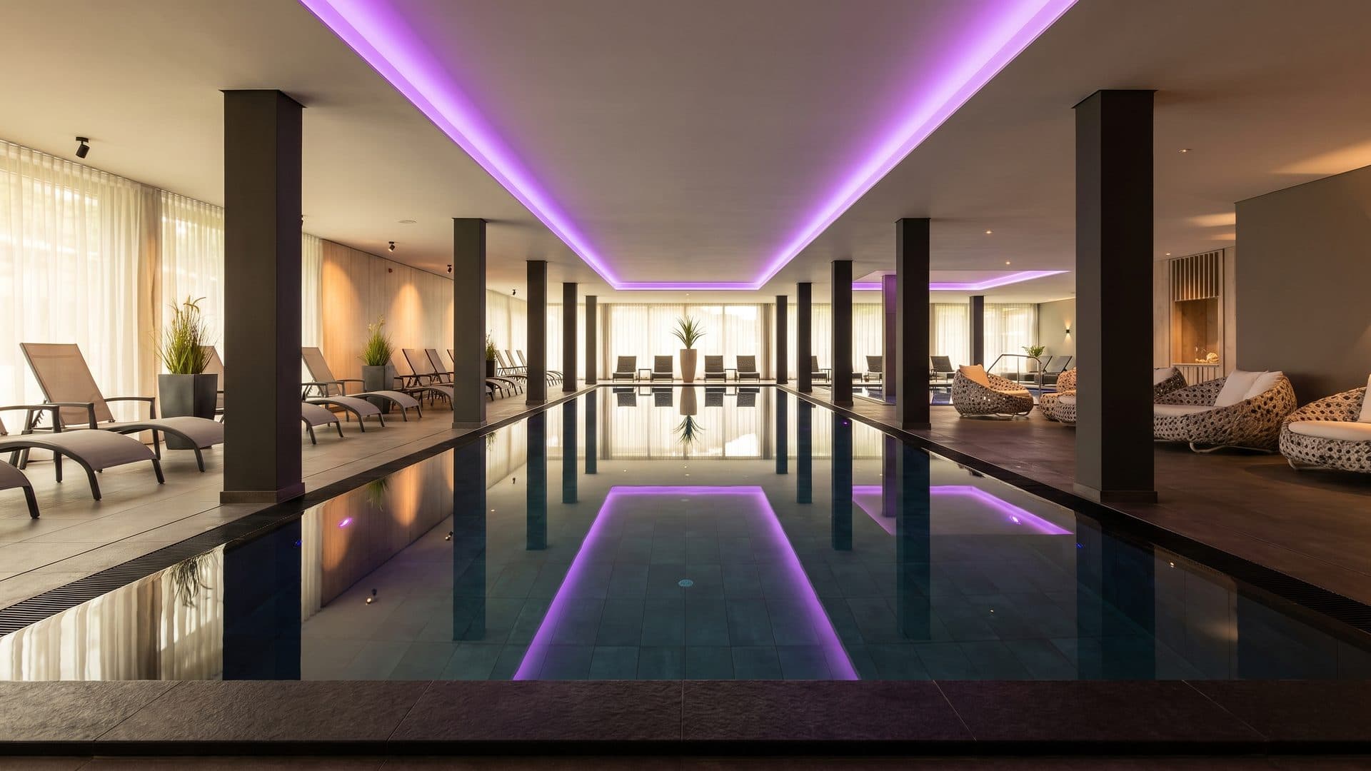 The indoor spa pool of Hotel Traube am See between dark columns under a lit ceiling