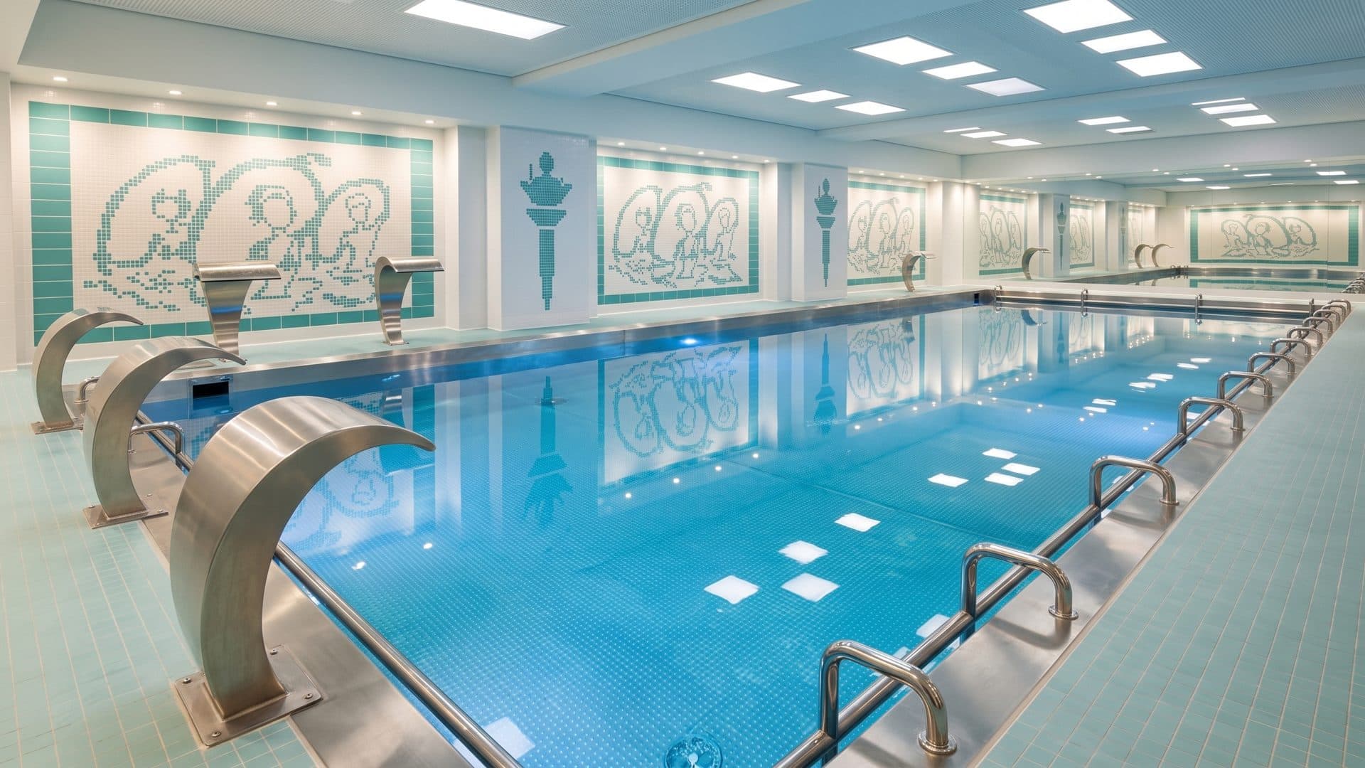 Indoor spa pool with water spouts along the wall and mosaic panels above them.
