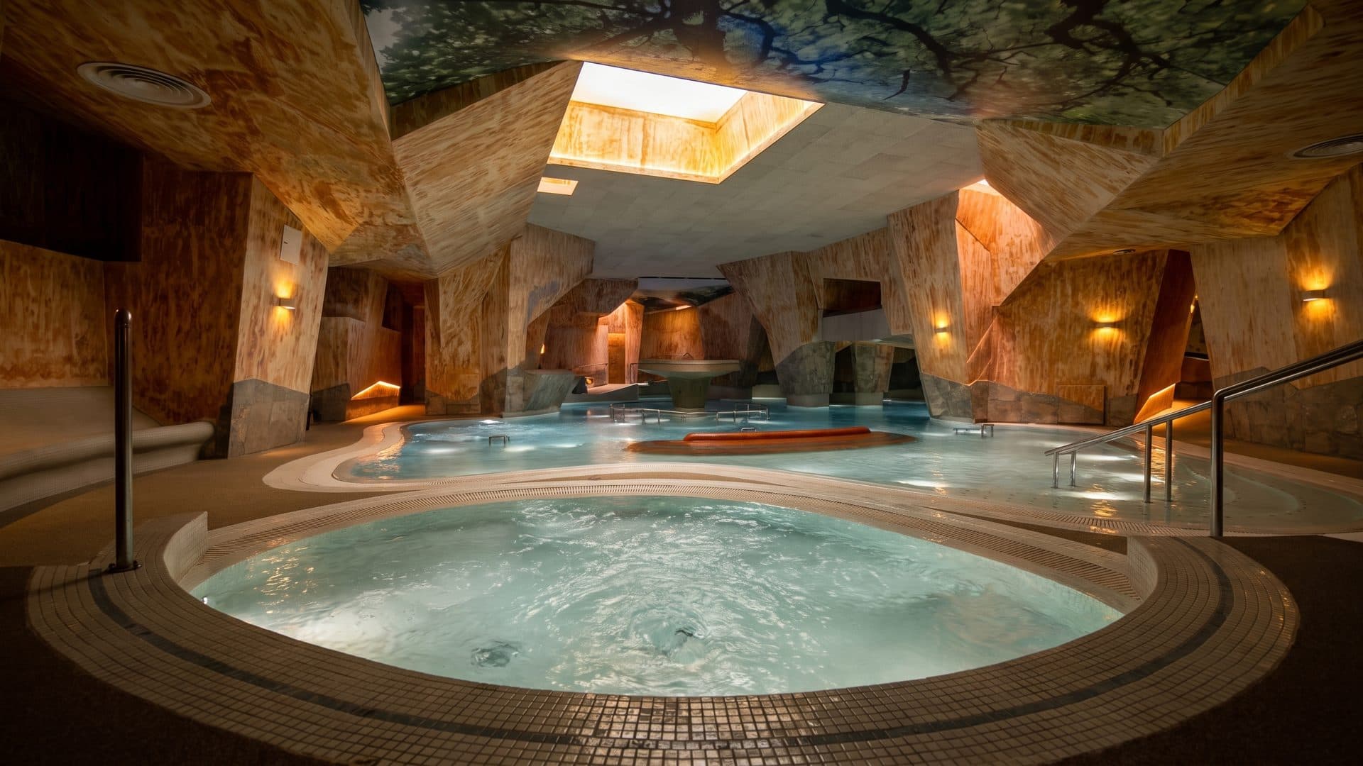 The rock-walled grotto hall at Viiking Saaga, a round bubbling pool in the foreground and daylight falling through an opening in the vault