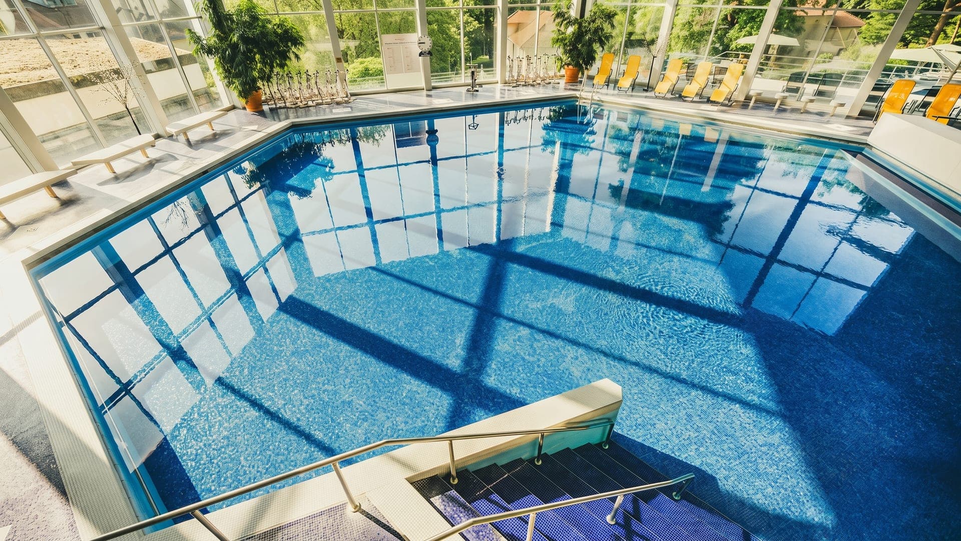 Indoor pool under a glass roof with yellow loungers along the edge