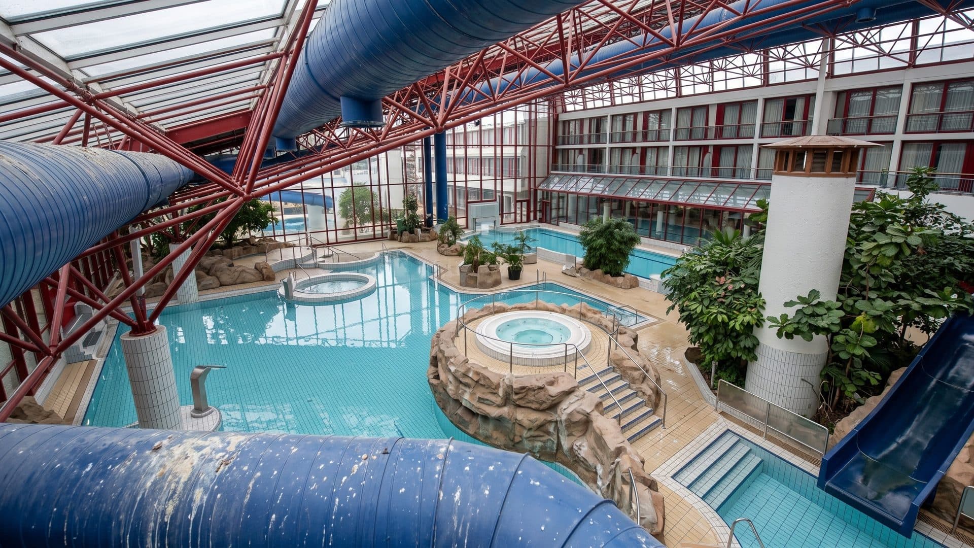 The indoor leisure pool of the Vitamar in Bad Lauterberg under a red steel roof, with a lighthouse tower and slides