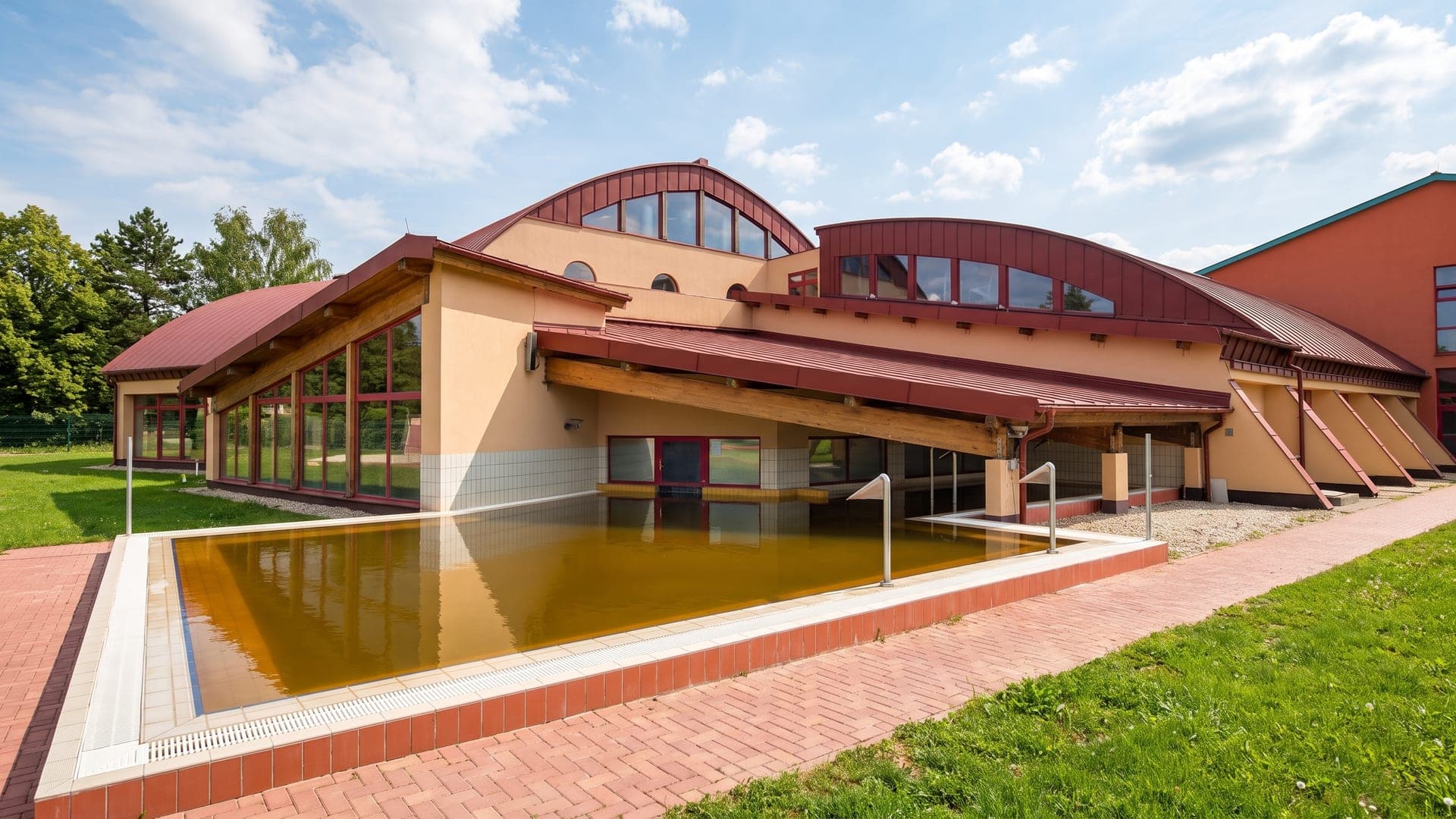 The outdoor pool at the Vulkan bath in Celldomolk, its green thermal water in front of the terracotta-roofed building.