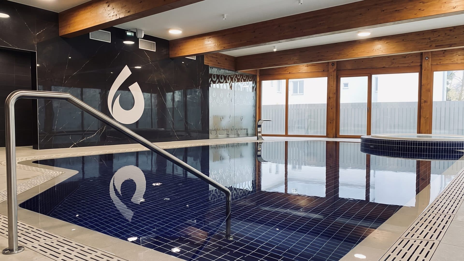 The dark-tiled indoor pool of Wellness Javor under its timber ceiling by the window wall