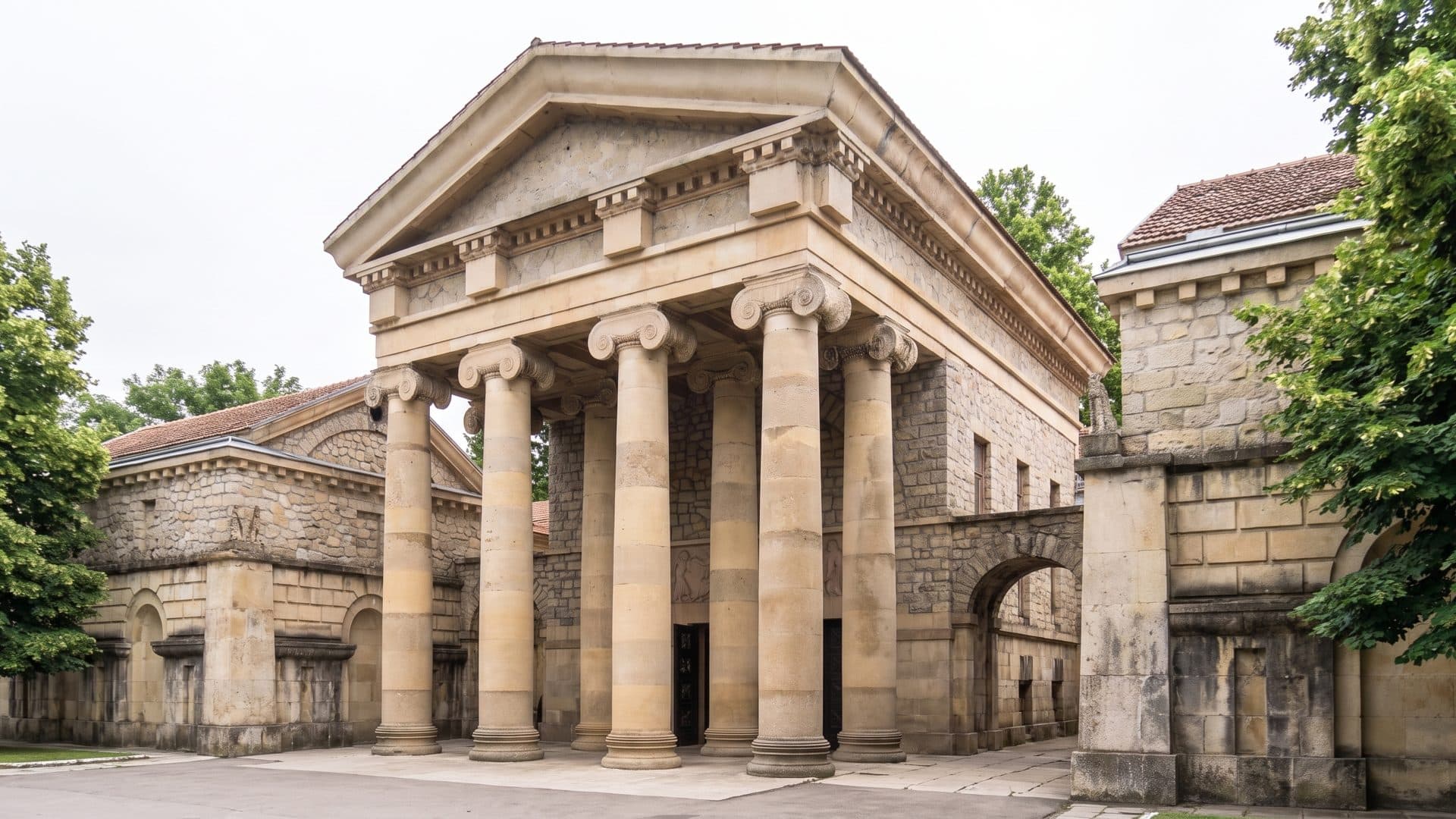 The sandstone portico of the Semashko mud baths in Yessentuki seen obliquely from the corner, its Ionic columns and rusticated side wings receding under a grey sky