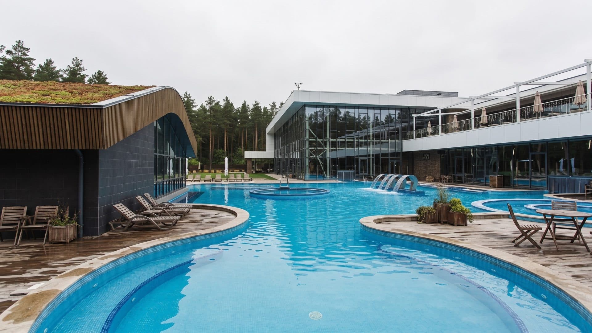 Curving outdoor pools of the YUGA spa before a glass building with a green roof, pine forest behind