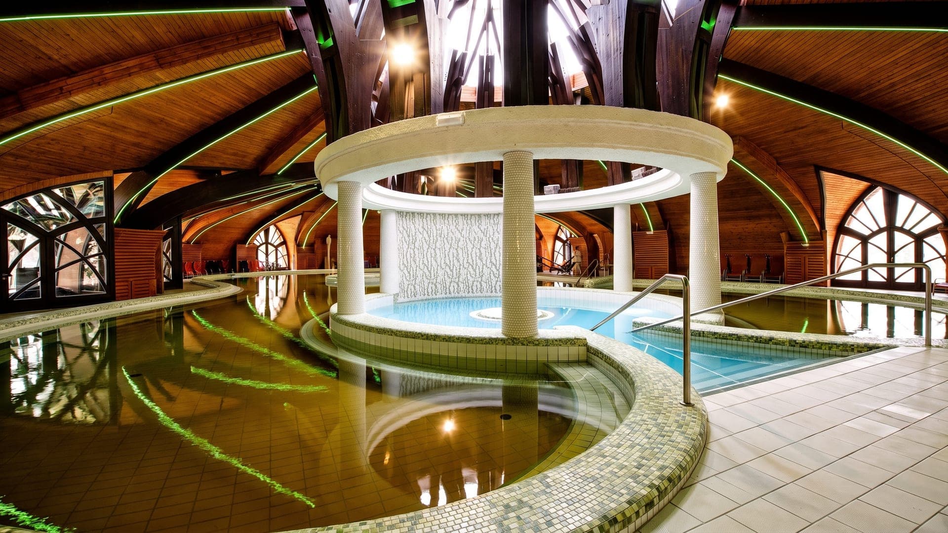 The indoor hall at the Zalakaros bath, its green mineral water under a timber vault carried on mosaic columns.