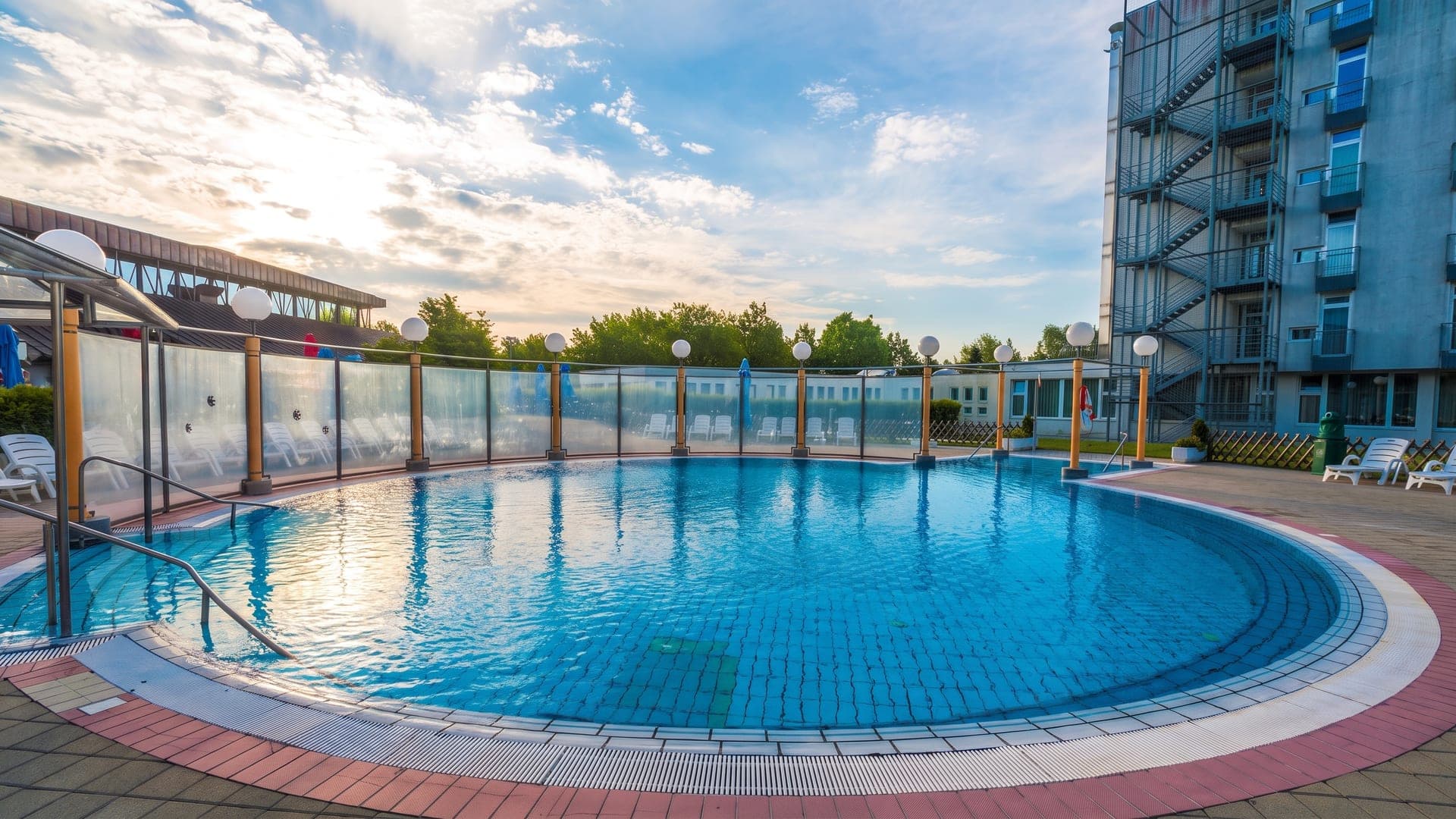 The round outdoor pool at the Radenci spa at dawn, beside the tall hotel block.