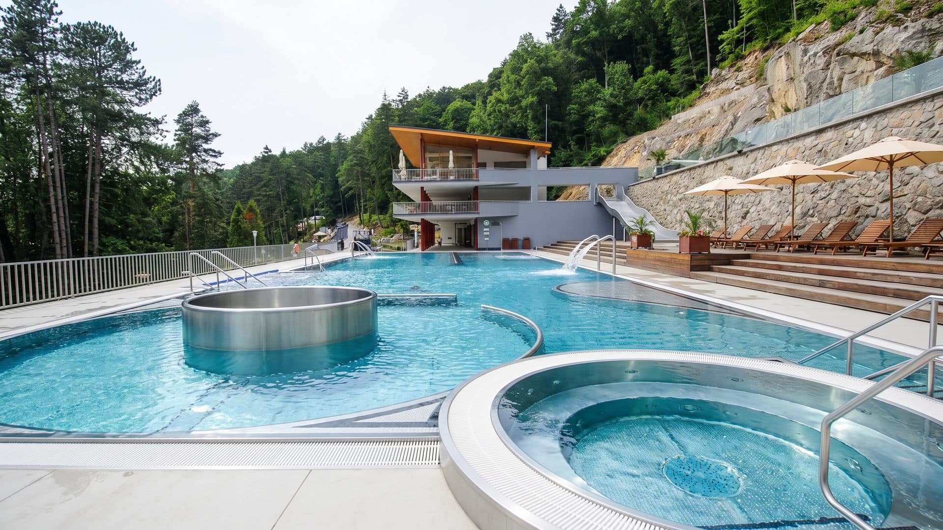 The terraced outdoor pools of the Zelena zaba lido below the rock face, with whirlpool basins set into the deck
