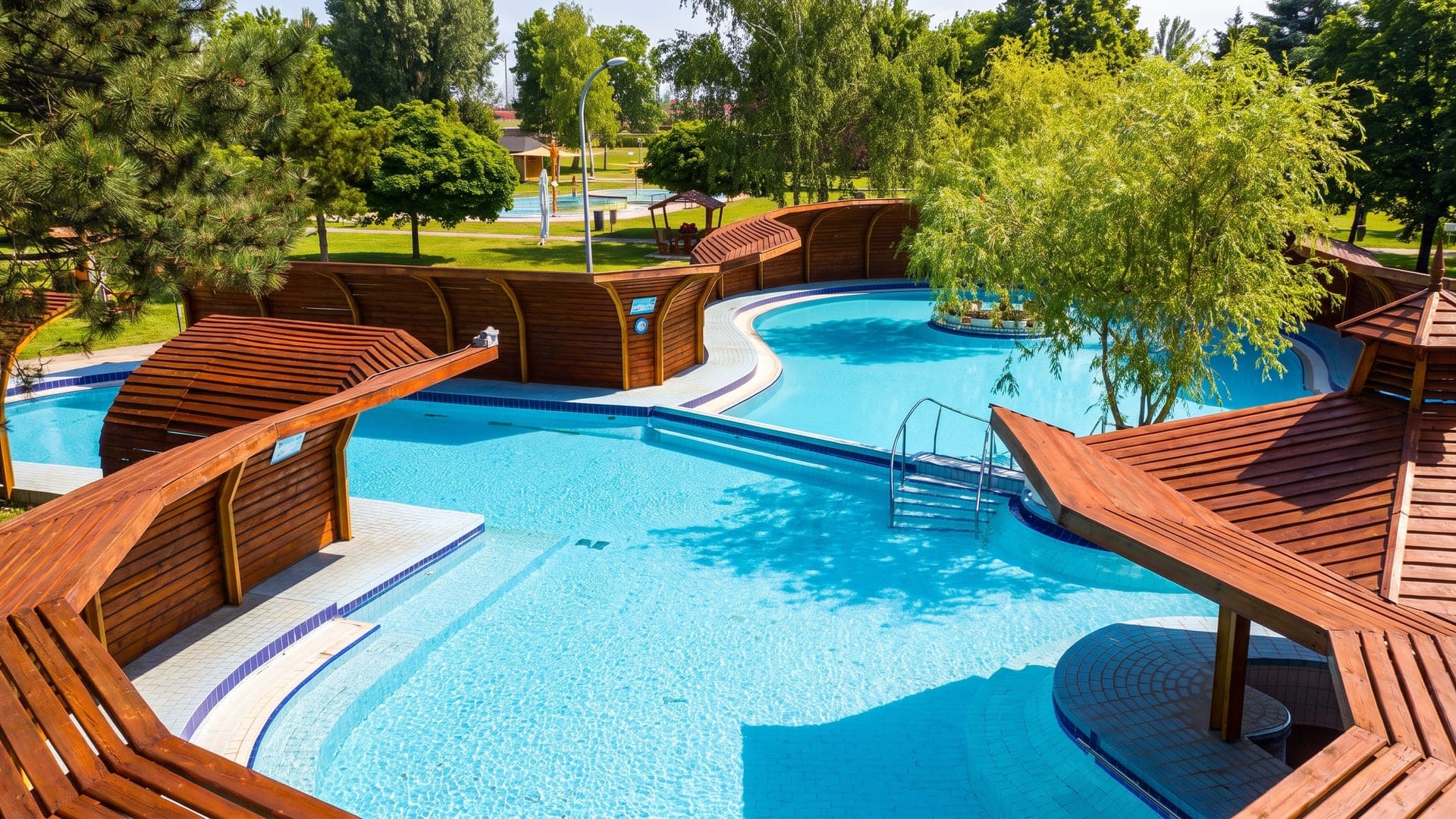 The outdoor pools at the Brigetio thermal bath in Komarom, their timber screens and terraces set in the park.