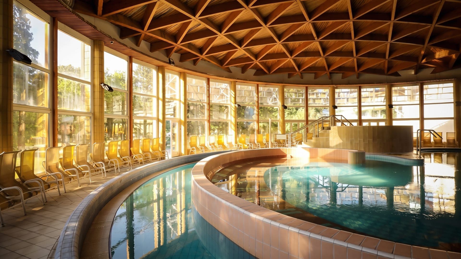 The indoor pool at the thermal bath in Buk, under a domed timber lattice roof with a wall of windows.