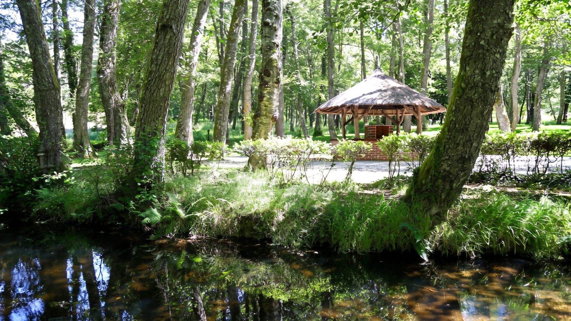 Thatched round pavilion in the spa park, standing among tall trees beside a clear stream.