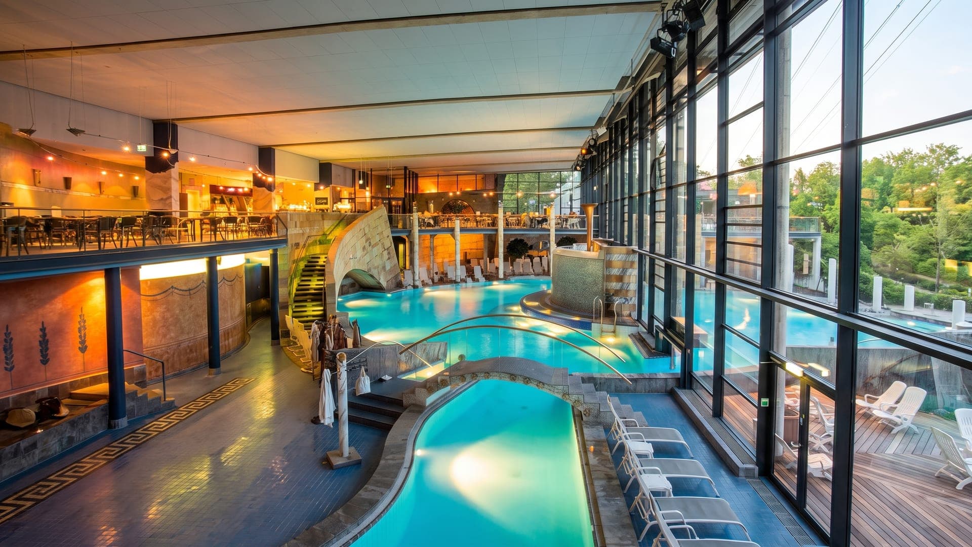 The bathing hall of the Claudius Therme in Cologne in the evening, with stone terraces and warm lighting above the water.