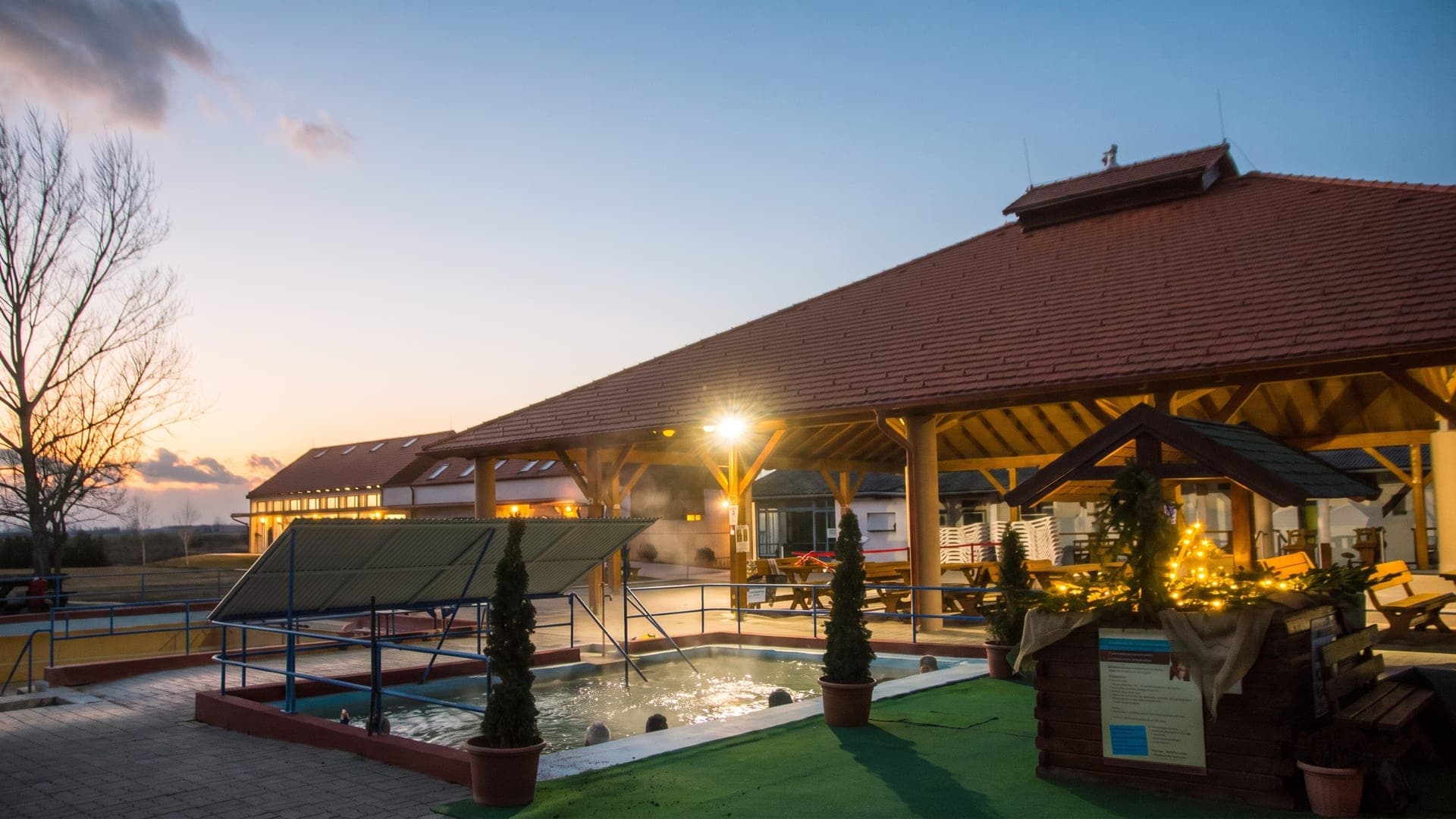 The timber pavilion over the pool at Csiszta Furdo in Buzsak at dusk, lit against the evening sky.