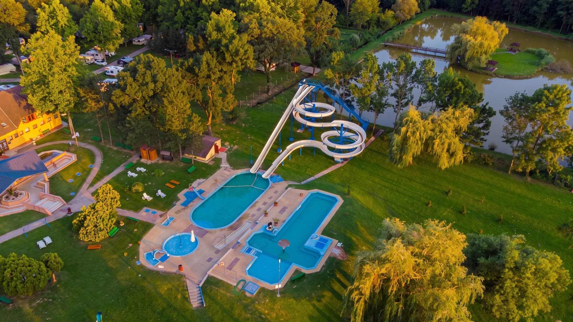 The thermal bath at Csokonyavisonta seen from the air, its pools and waterslide among willows beside a pond.