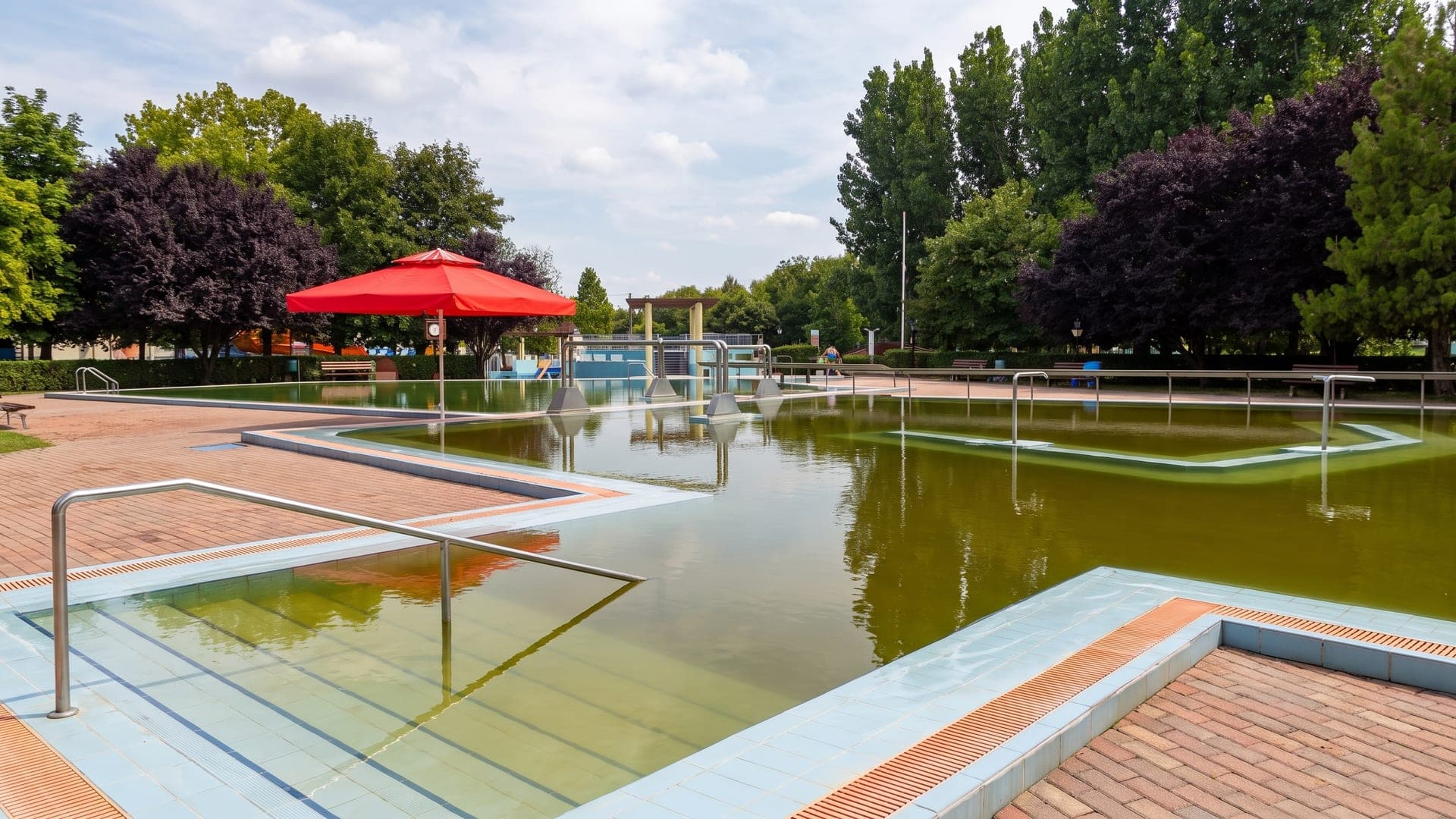 The outdoor thermal pool at the bath in Davod, its green mineral water edged with brick paving and parasols.