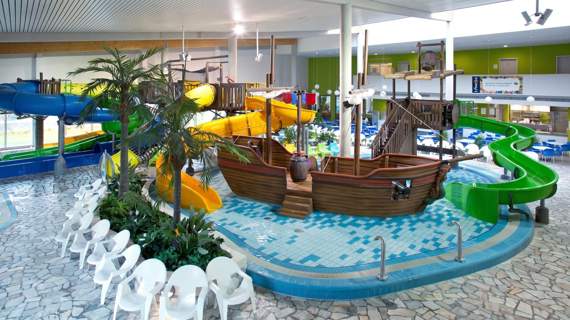 The indoor family pool at Fuerthermare in Fuerth, with a wooden pirate ship, palms and coloured slides.