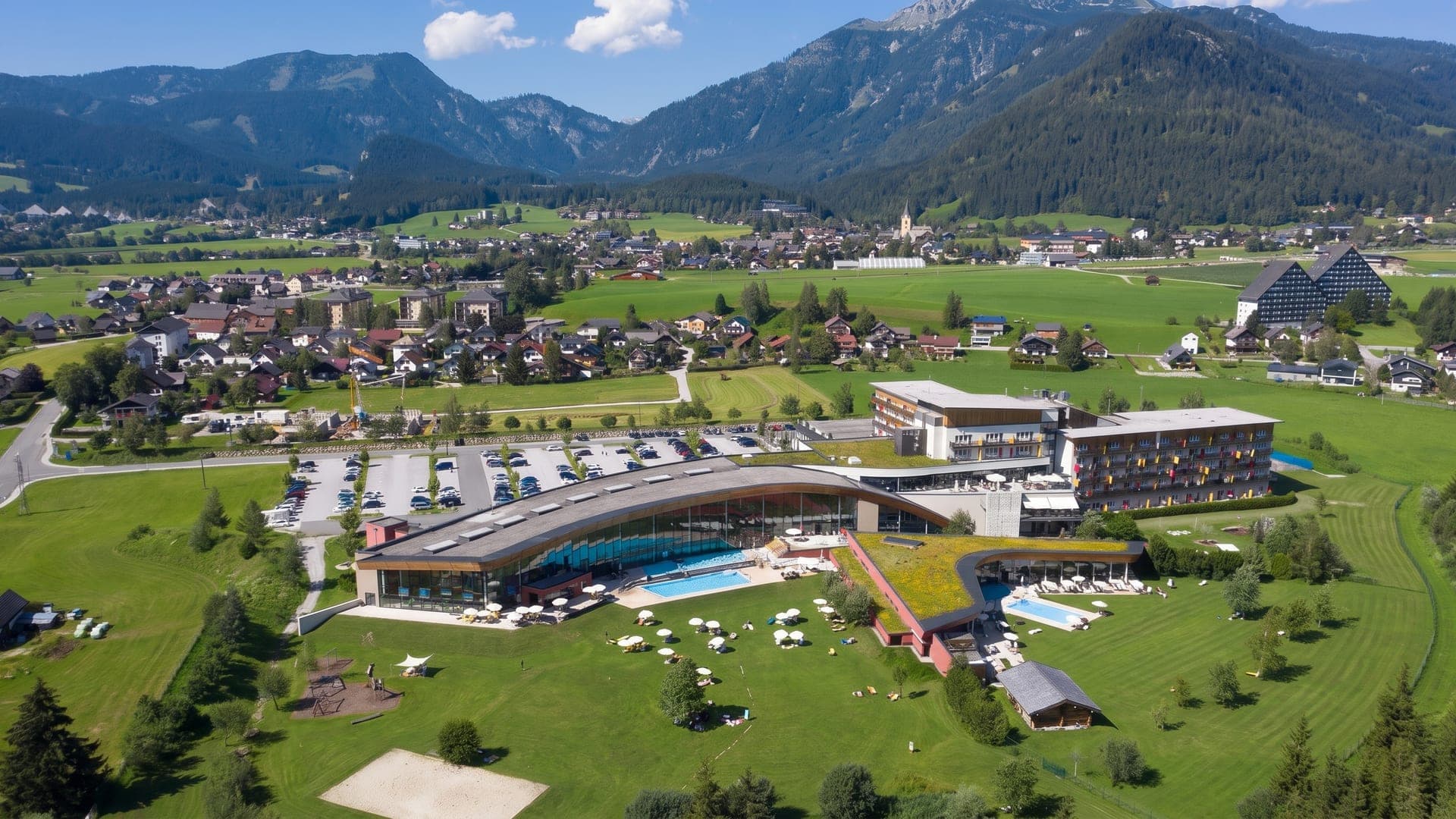 The GrimmingTherme seen from the air, its pools and green-roofed hall in the meadows of the Bad Mitterndorf valley below the peaks.