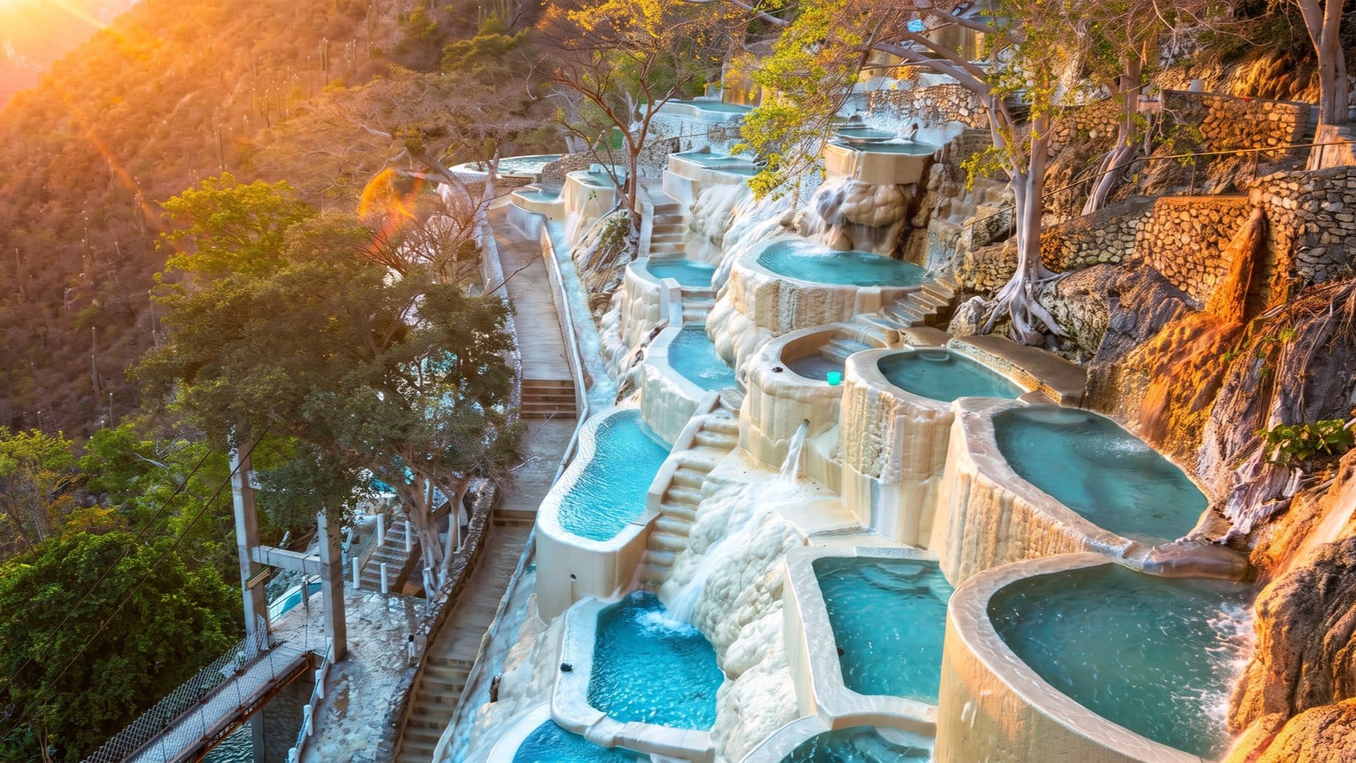 Rows of turquoise pools set into pale travertine terraces on the canyon wall, lit gold by a low sun.