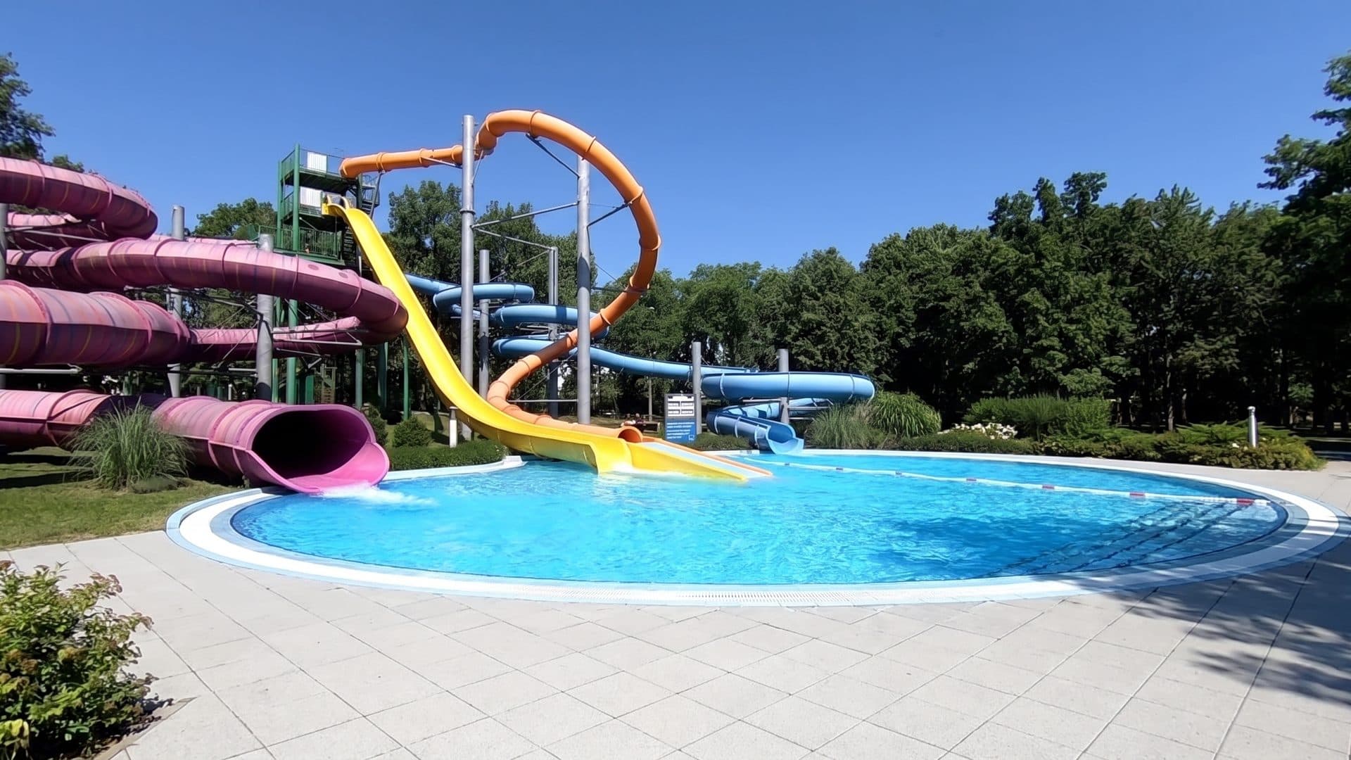 The outdoor pool of the Hullamfurdo with its slide tower and deck among the trees