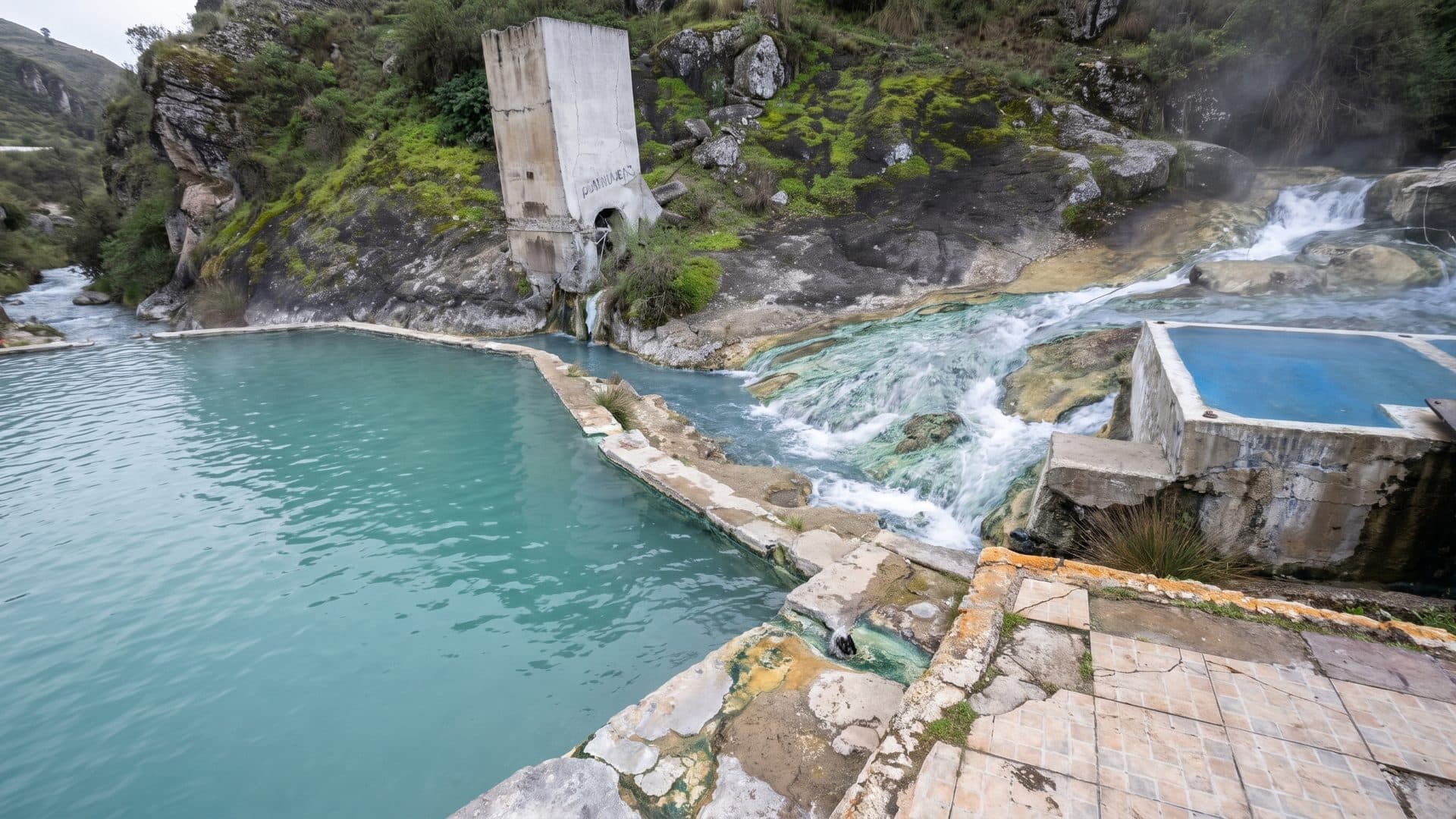 Turquoise hot spring pools below a travertine bank, steam rising where the water falls.
