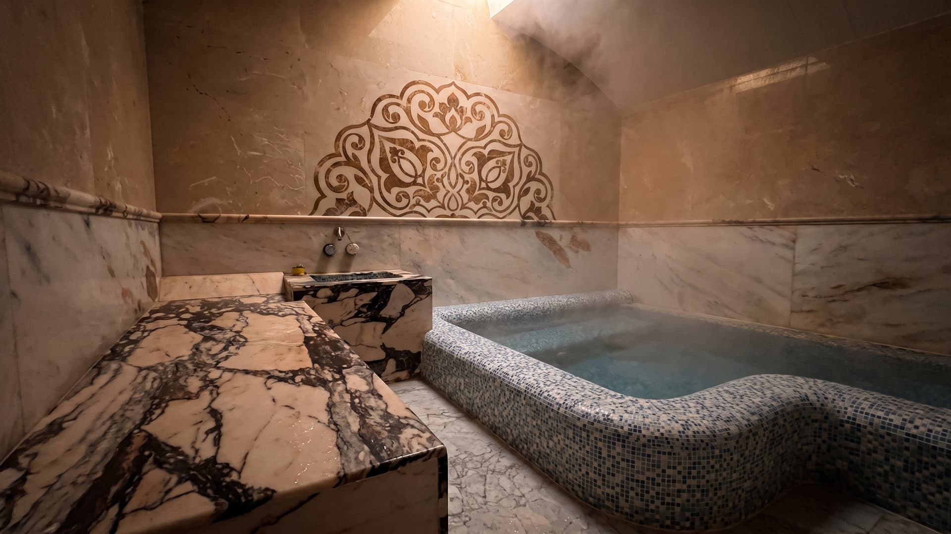 Marble bathing room with a mosaic-lined plunge pool and a carved ornament high on the wall above it.