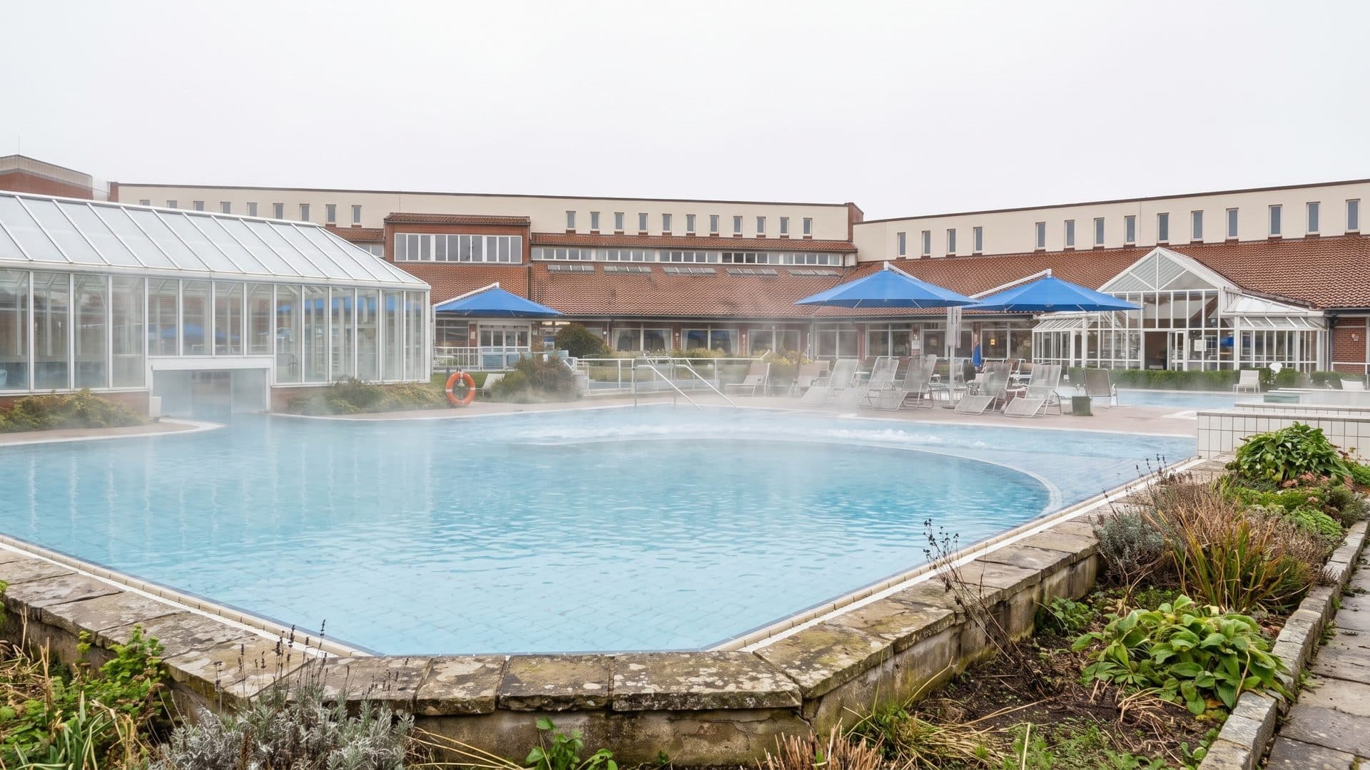The steaming outdoor thermal pool at the Limestherme, with the glazed bath hall and terrace behind it