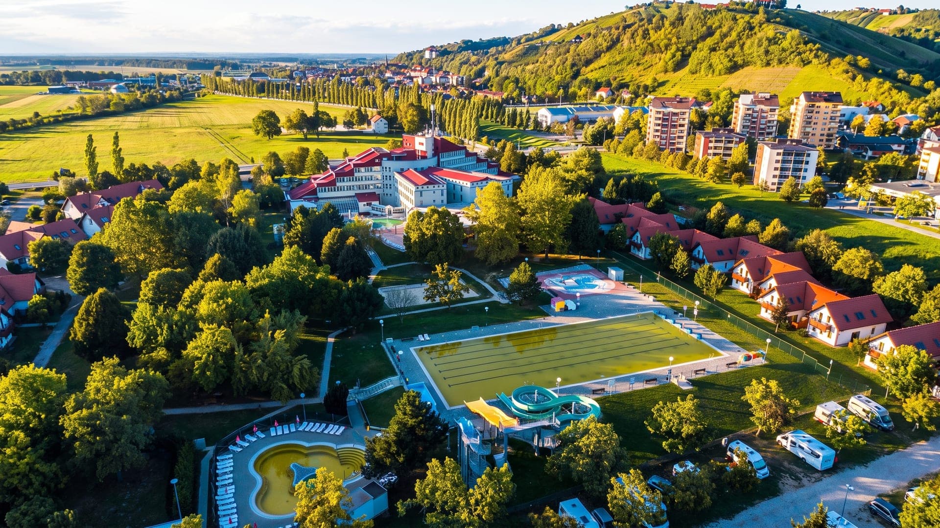 Terme Lendava seen from the air, its pools and buildings among trees with the vineyard hills beyond.