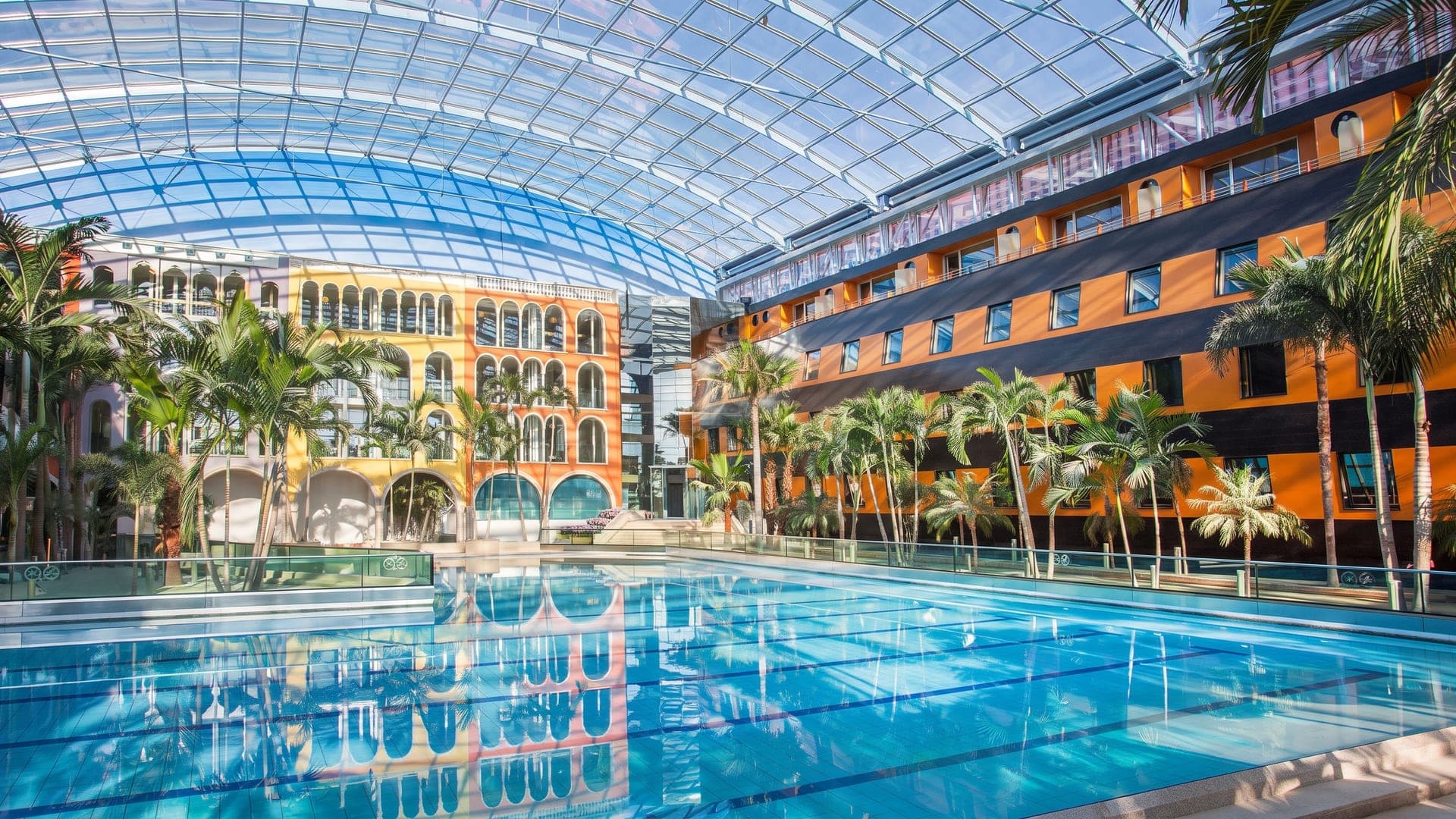 The palm hall at Therme Erding in the evening, its pool beneath the arched glass roof with the galleries lit warm.