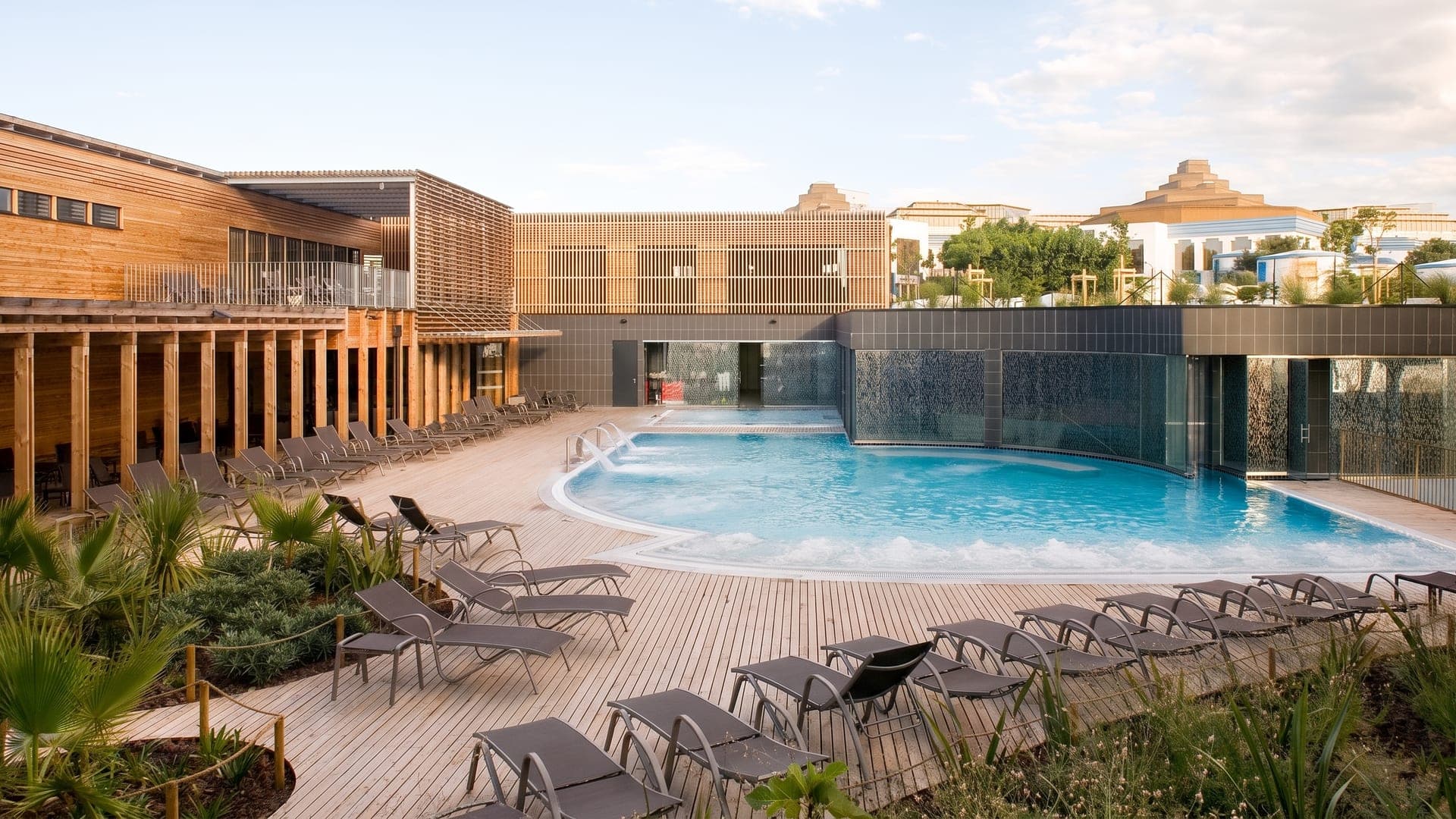 The outdoor pool at the Thermes de Balaruc beside the timber-clad building, with loungers on the deck.