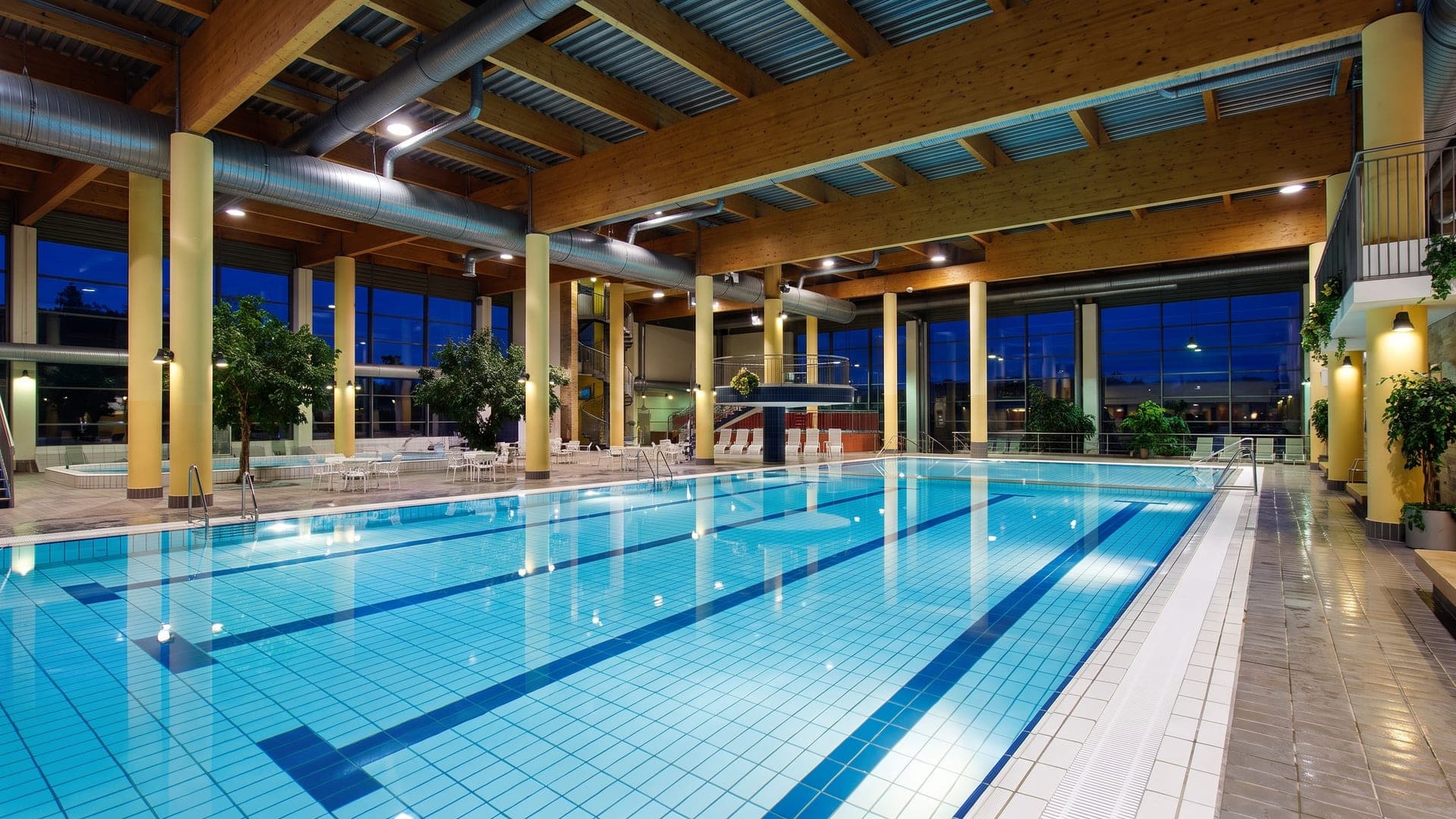 The indoor hall at the Thueringentherme in Muehlhausen, its lane pool under a timber roof with a glass wall onto the park.