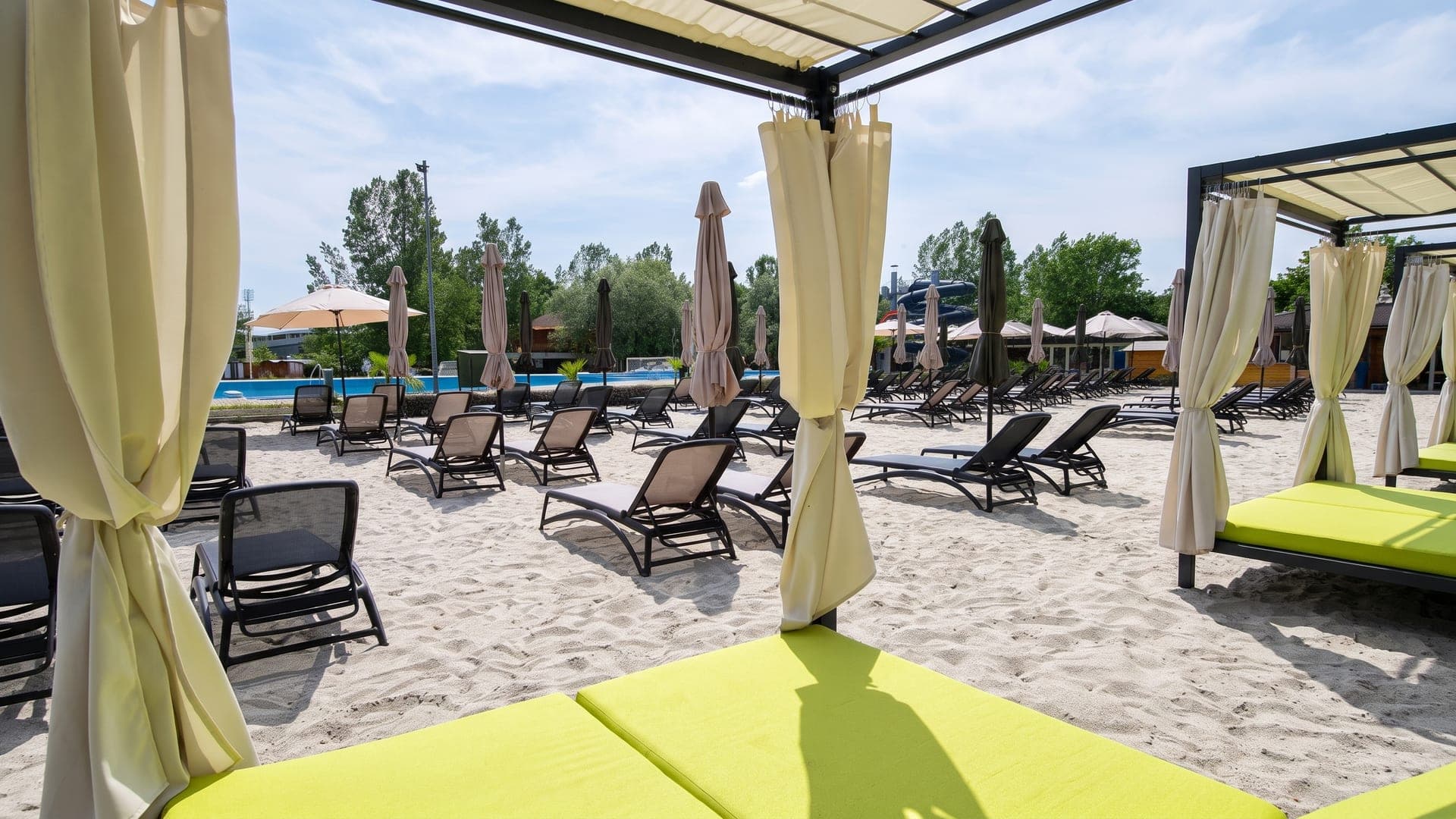 The sand beach at Varkert Furdo in Papa, with loungers and curtained cabanas beside the outdoor pool.