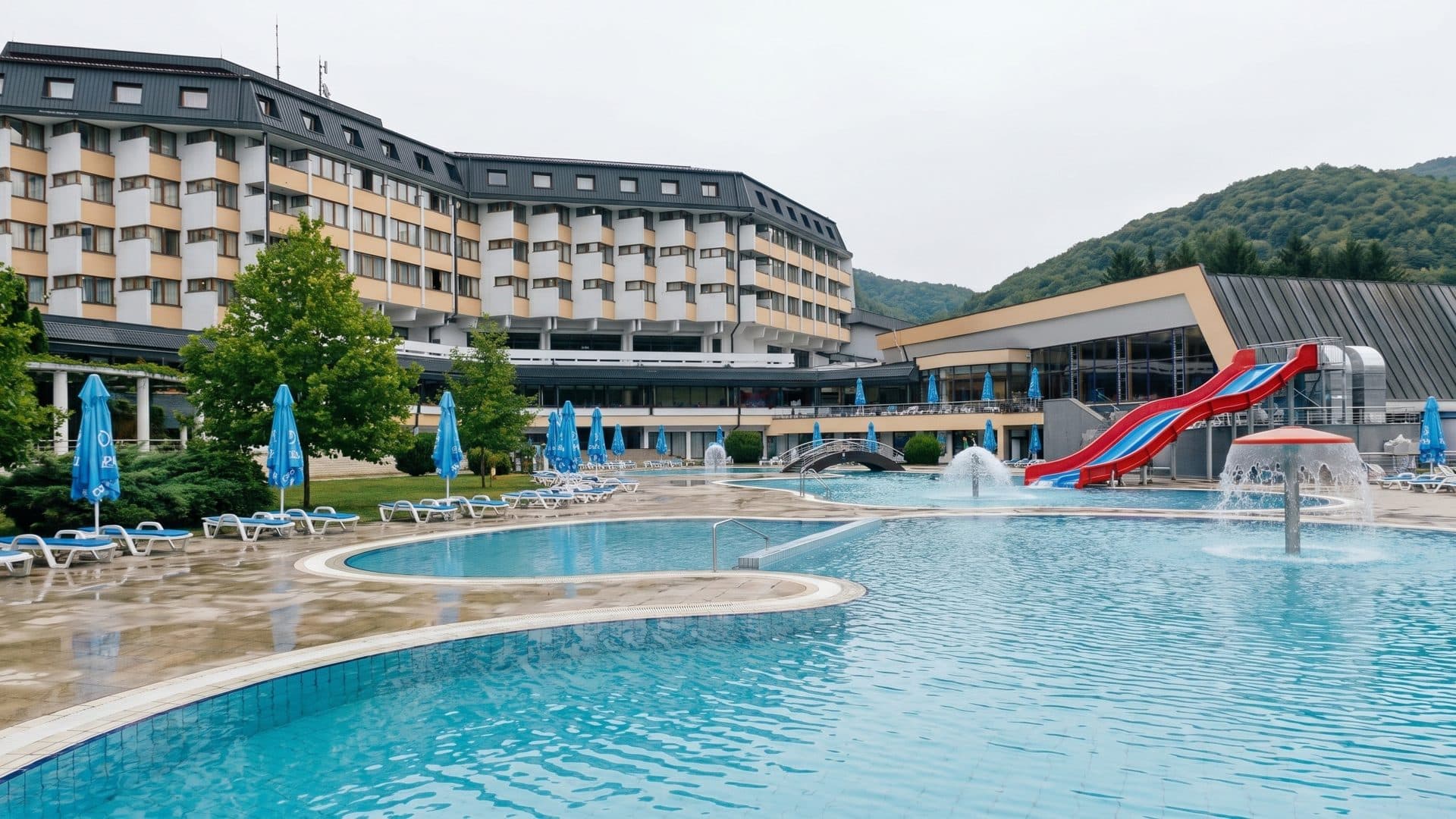 The outdoor pool at Vrucica in front of the terraced hotel block, with red and blue slides and parasols along the deck